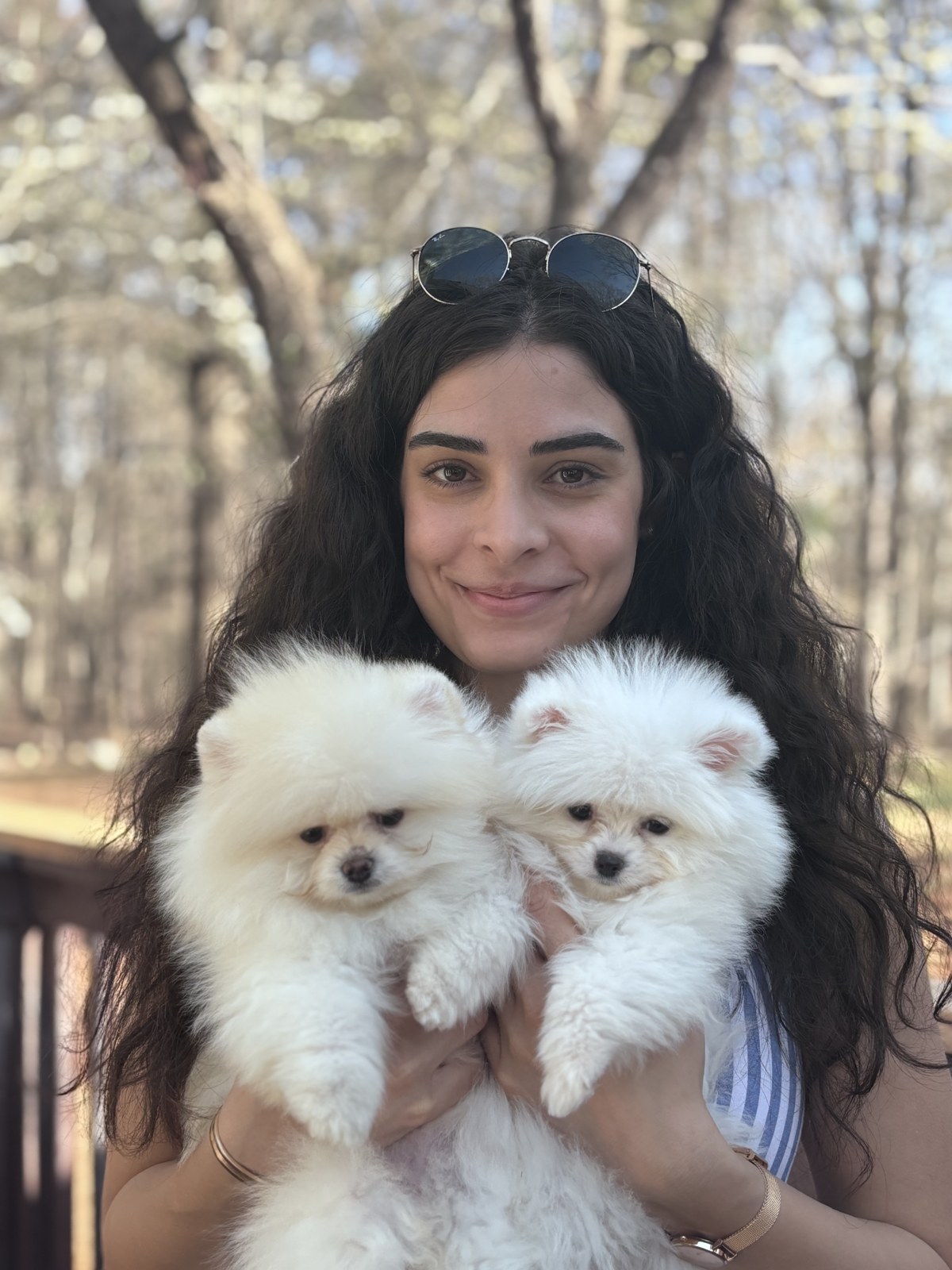 Milana holding two fluffy white Pomeranian puppies outdoors